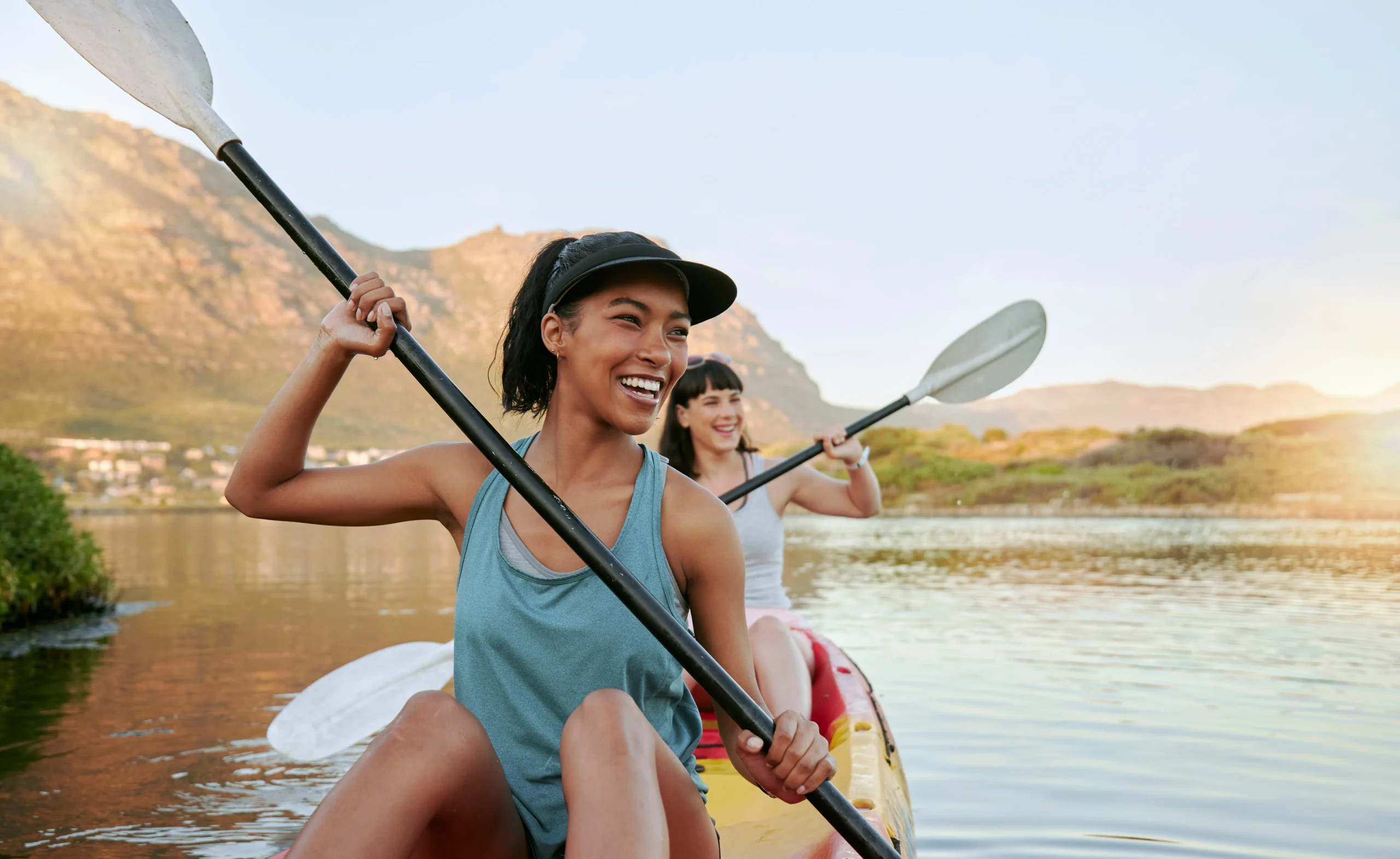two women smiling while they kayak down a river